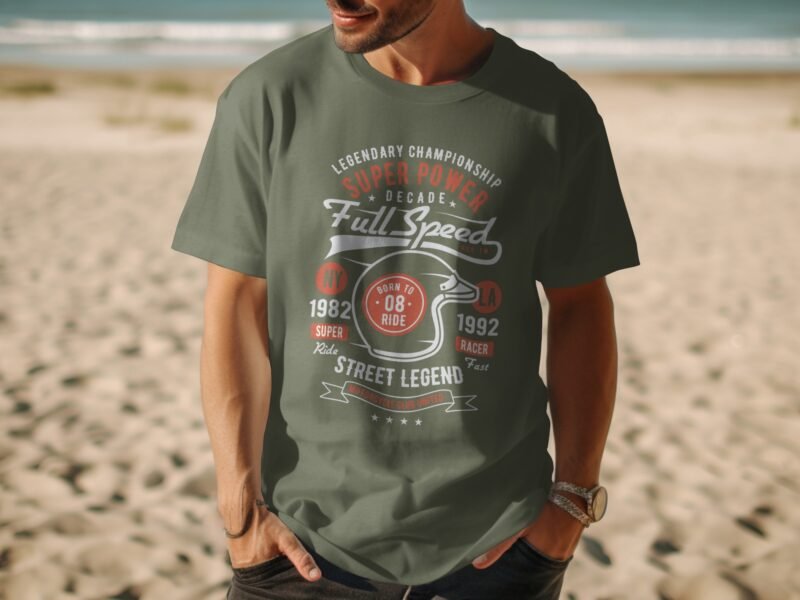 Man wearing a green t-shirt with racing graphic design, standing on a sandy beach, ocean in the background.