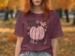 A person wearing a maroon shirt with a pink pumpkin graphic, set against a backdrop of autumn leaves.