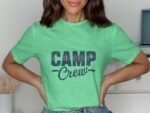 A woman wearing a green t-shirt with "CAMP Crew" printed in dark blue letters, smiling and posing with hands on hips.
