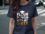 A person wearing a navy blue t-shirt with the text "FLOUR POWER - LET'S GET DIRTY" in bold, playful fonts.