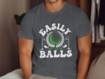 A person wearing a gray t-shirt with "Easily Distracted By Balls" graphic featuring a golf ball and clubs.