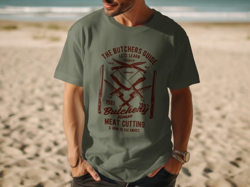 A man wearing a green t-shirt with a retro butchery graphic stands on a beach with waves in the background.
