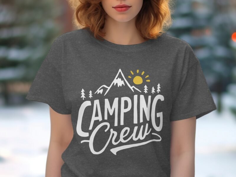 Person wearing a gray t-shirt with "Camping Crew" design featuring mountains, trees, and a sun in a natural setting.