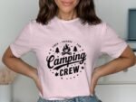 A woman in a pink t-shirt featuring the text "Camping Crew" and campfire graphics, smiling and posing indoors.