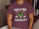 A person wearing a maroon t-shirt with the text "Golfing Cheaper Than Therapy" and a graphic of a golf ball.