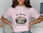 Woman wearing a pink t-shirt with a graphic of mountains and a camper, text reads "Let's Get Lost Adventure Awaits."