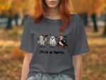 A woman with reddish hair wears a gray t-shirt featuring cartoon chickens and a ghost, saying "Chick or Tweet."