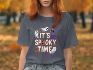 Woman in a gray shirt with "It's Spooky Time" graphic, featuring ghosts and pumpkins, set against an autumn background.