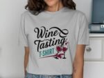 A woman in a gray t-shirt with "Wine Tasting T-SHIRT" graphic and wine glasses design, smiling in a home setting.