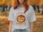 A person in a grey t-shirt with a pumpkin graphic and text reading "If you’ve got it, haunt it," against a fall background.