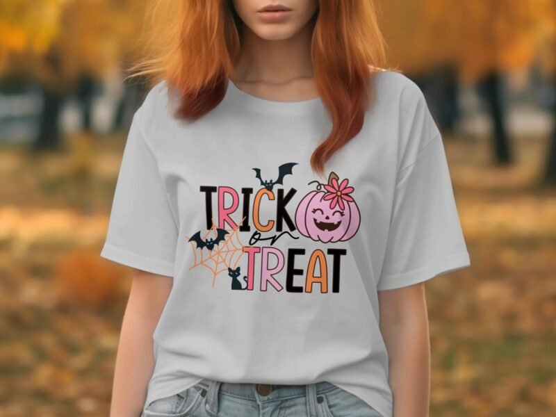 A woman with red hair wears a light gray t-shirt featuring "TRICK or TREAT" with Halloween graphics against an autumn backdrop.