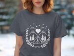 A woman models a charcoal gray t-shirt featuring a white graphic of mountains, trees, a tent, and a heart.