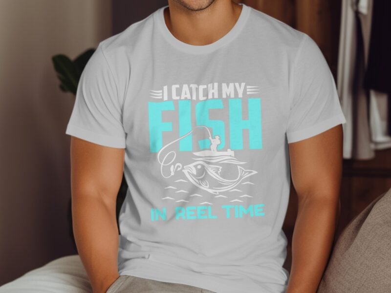 A person wearing a light gray t-shirt with blue text that reads "I CATCH MY FISH IN REEL TIME" over a fishing graphic.