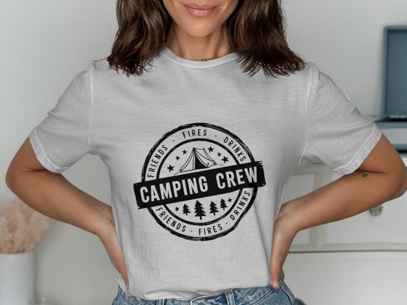 Woman wearing a light gray t-shirt with a "Camping Crew" design featuring a tent and trees, posing against a neutral background.