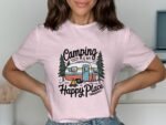A woman in a pink t-shirt featuring a camping design with a camper, trees, and the text "Camping is my Happy Place."