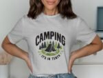 A woman wears a gray t-shirt featuring "CAMPING" and a tent graphic surrounded by trees and the phrase "IT'S IN TENTS."