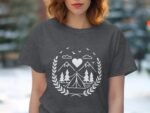 Woman with medium-length wavy hair wearing a dark gray t-shirt featuring a white camping-themed graphic design.