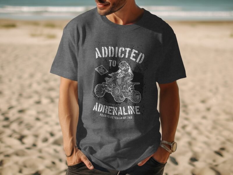 Man wearing a gray t-shirt with "Addicted to Adrenaline" graphic, standing on a sandy beach with ocean in background.