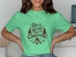 Model wearing a green t-shirt with "Life is Better Around the Campfire" graphic surrounded by trees and a campfire design.
