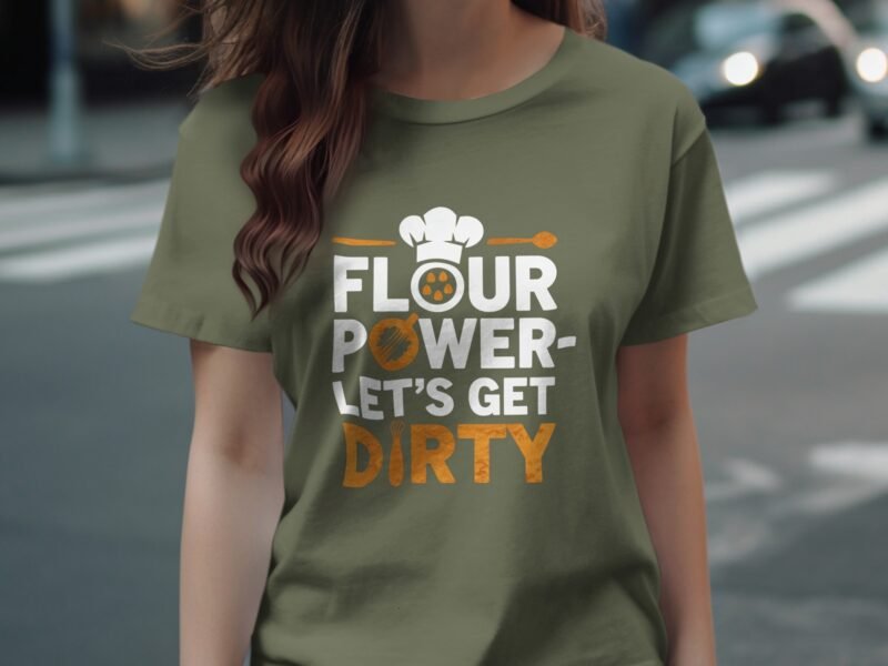 A woman in an olive green t-shirt with the text "FLOUR POWER- LET'S GET DIRTY," featuring a chef's hat and whisk graphic.