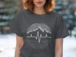 A woman with wavy hair wears a dark gray shirt featuring a mountain and heartbeat line graphic.