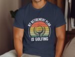 A man wearing a navy t-shirt with the text 'MY RETIREMENT PLAN IS GOLFING' and a graphic of a golf ball.