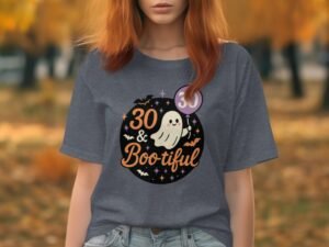 A woman in a gray t-shirt with a ghost graphic reads "30 & Bootiful," surrounded by autumn trees.