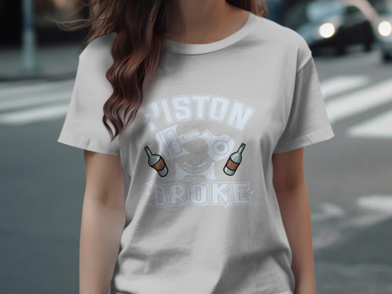 A woman in a light gray t-shirt with the words "PISTON BROKE" and two bottle graphics stands on a street.