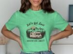 Woman wearing a green t-shirt with the phrase "Let's Get Lost" and a camper graphic amid mountains and trees.