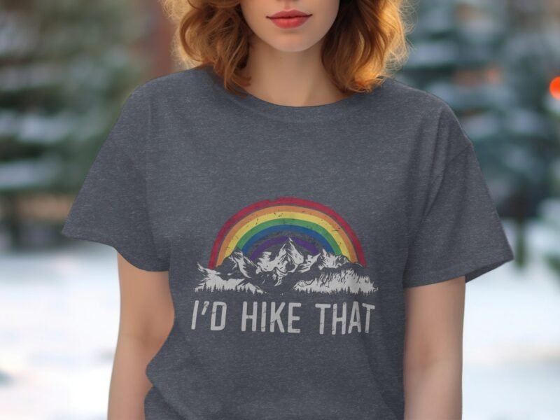 A woman in a gray t-shirt featuring a rainbow and mountains, with the text "I'd hike that" printed below.