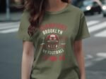 A person wearing an olive green t-shirt with a vintage football design and text reading "Champions Brooklyn 1988."