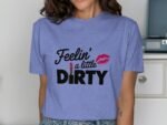 Woman in a lavender shirt with "Feelin' a little DIRTY" graphic and lipstick illustration, smiling.