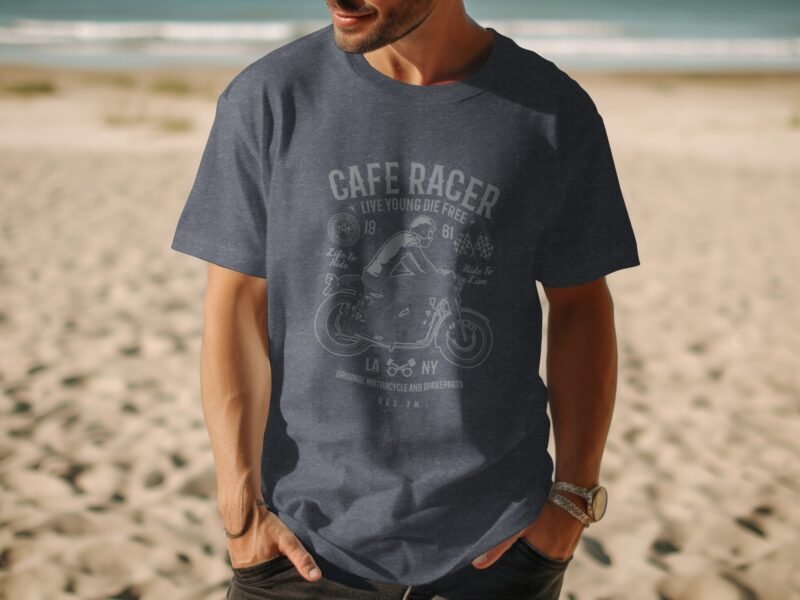 A man wearing a navy t-shirt with a vintage motorcycle design stands on a sandy beach with ocean waves in the background.