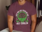 Person wearing a maroon t-shirt with green golf-themed graphic and text: "GOLF KID LIKE REGULAR KID BUT COOLER."