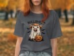 A woman in a gray t-shirt with a cartoon cow in a ghost costume, holding a pumpkin, surrounded by bats.
