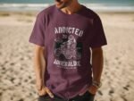 A man stands on a beach wearing a purple t-shirt with a graphic reading "Addicted to Adrenaline."