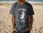 Man wearing a dark gray t-shirt with a vintage-style graphic that says "Hard Work Never Give Up" on a beach.