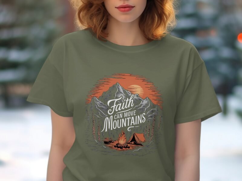 A woman wears an olive green t-shirt featuring a mountain graphic with the words "Faith Can Move Mountains" and a campfire.
