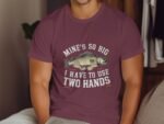 A person wearing a maroon t-shirt with a fishing graphic and text: "Mine's so big I have to use two hands."