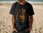 A man wearing a black t-shirt featuring a vintage truck graphic and the text "Classic Garage" on a beach.