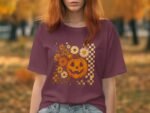 A person with red hair wears a maroon t-shirt featuring a floral jack-o'-lantern design, surrounded by autumn leaves.