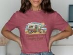 A woman in a maroon t-shirt with a camping-themed graphic, smiling with hands on her hips, in a bright indoor setting.