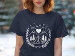 A woman in a navy t-shirt featuring a white camping-themed graphic with mountains, trees, a tent, and a heart.