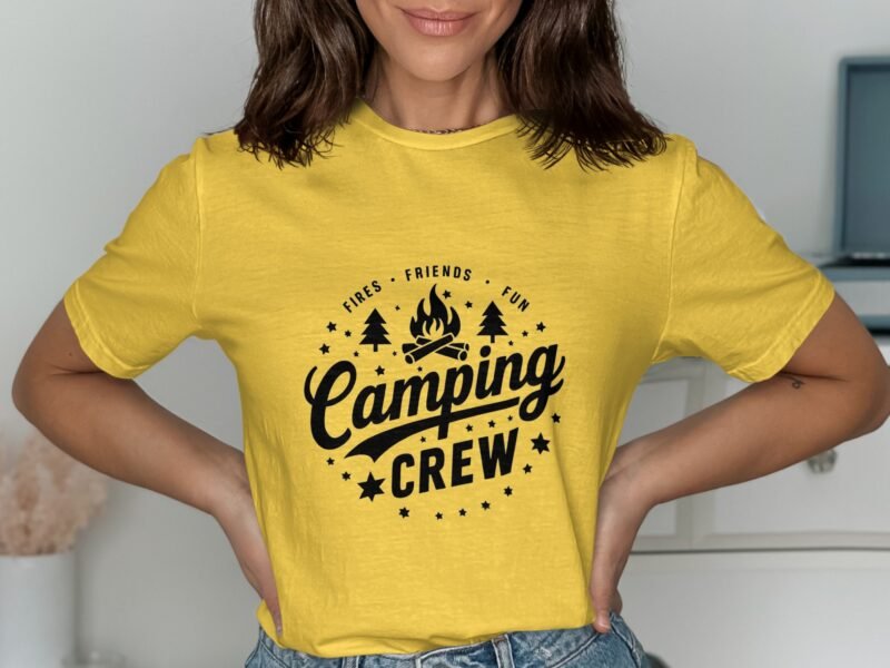 A woman wearing a yellow t-shirt with a black "Camping Crew" graphic, posing playfully with hands on hips.