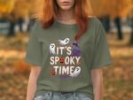 A person in a green shirt with "It's Spooky Time" graphic, featuring ghosts, pumpkins, and a haunted house, in a fall setting.