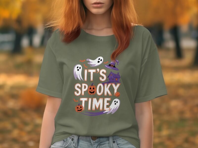 A person in a green shirt with "It's Spooky Time" graphic, featuring ghosts, pumpkins, and a haunted house, in a fall setting.