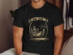 A person in a black t-shirt with a fishing graphic sits casually, looking relaxed in a cozy indoor setting.