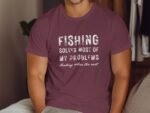 A person wearing a maroon t-shirt with the text "Fishing solves most of my problems. Hunting solves the rest."