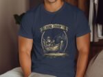 A man wearing a navy t-shirt with a vintage fishing graphic and the text "Gone Fishin'" sits indoors.