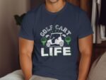 A man wearing a navy shirt with "GOLF CART LIFE" text and golf-themed graphics, seated indoors.
